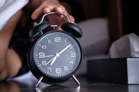 A modern alarm clock sitting on a bedroom nightstand beside a lamp