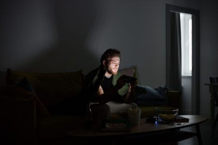 Bungie’s Marathon Silence Is Pulling Fans Back to Destiny 2 Raids A gamer sitting in a dark room illuminated by monitor light, focused on screen
